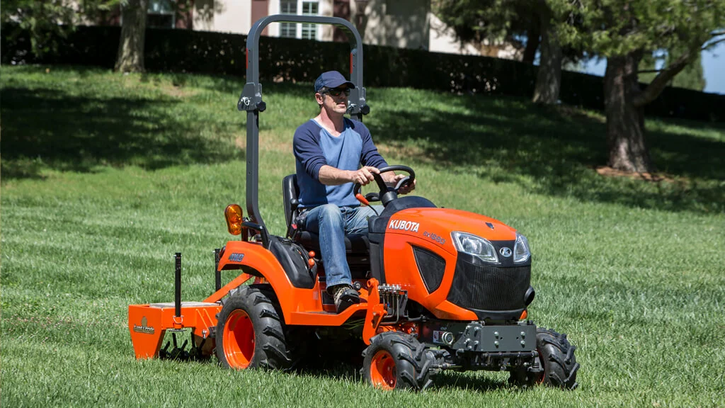 Operator mowing a lawn on an orange Kubota compact tractor fitted with a mid-mount mower deck
