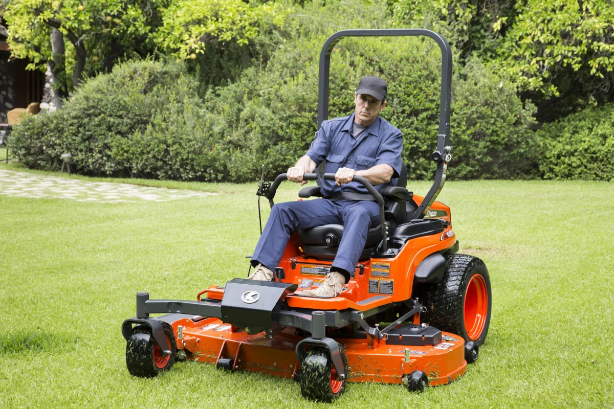 Operator on an orange Kubota zero-turn mower with a wide cutting deck on a garden lawn