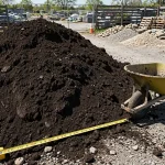 Pile of bulk topsoil at a landscape supply yard with a wheelbarrow